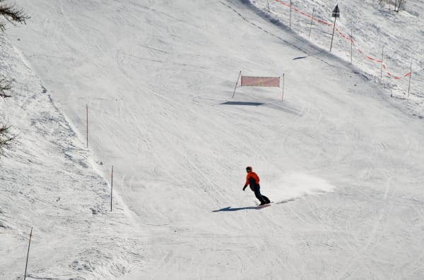 A snowboarder wearing orange descends a snowy slope on a clear winter day, capturing the essence of outdoor adventure.