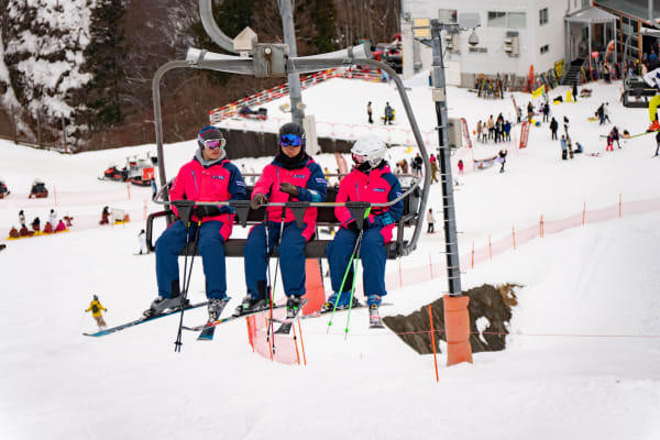 Three skiers in bright jackets on a chairlift in Yuzawa, Japan