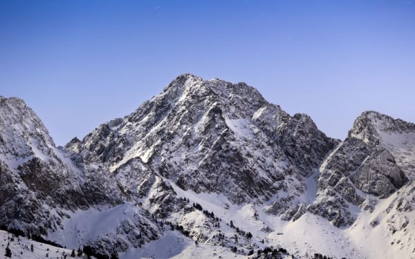 Breathtaking view of snow-covered mountains under a clear blue sky at sunrise, capturing winter's serene beauty.
