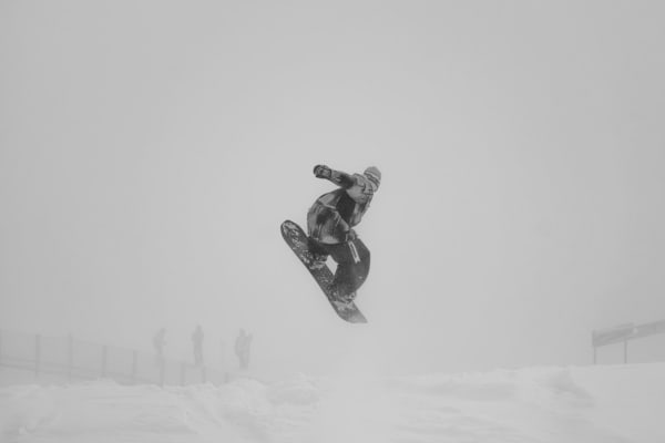 Snowboarder executing an aerial jump at a funpark in Mayrhofen, Austria, amidst foggy winter landscape.