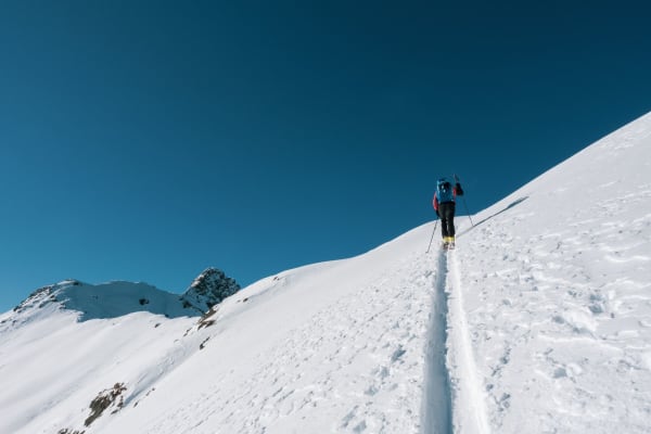 Person skiing on a snowy mountain slope under clear blue sky in winter.