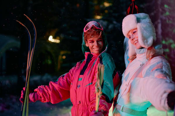 Two friends in vibrant 80s winter fashion, celebrating a night skiing adventure.