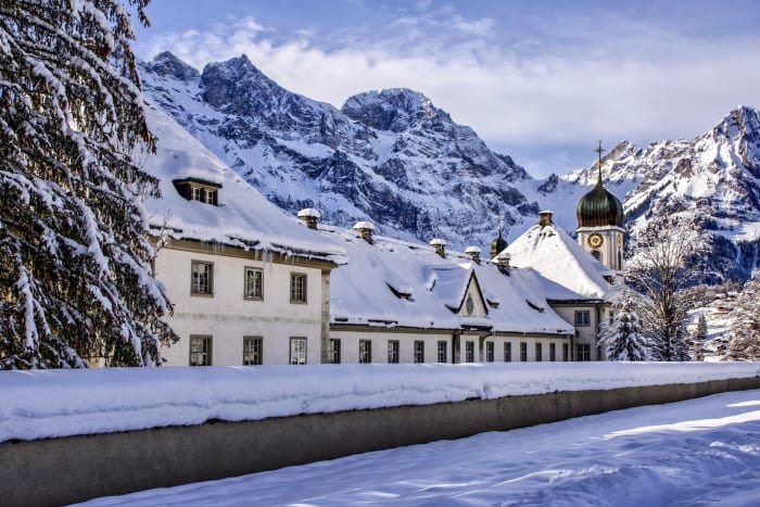 A picturesque Bavarian church nestled in a snow-covered landscape, framed by majestic mountains under a bright winter sky.