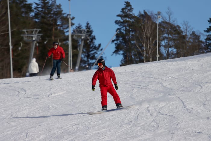 A snowboarder in a red suit riding a sunny slope near Jönköping, Sweden