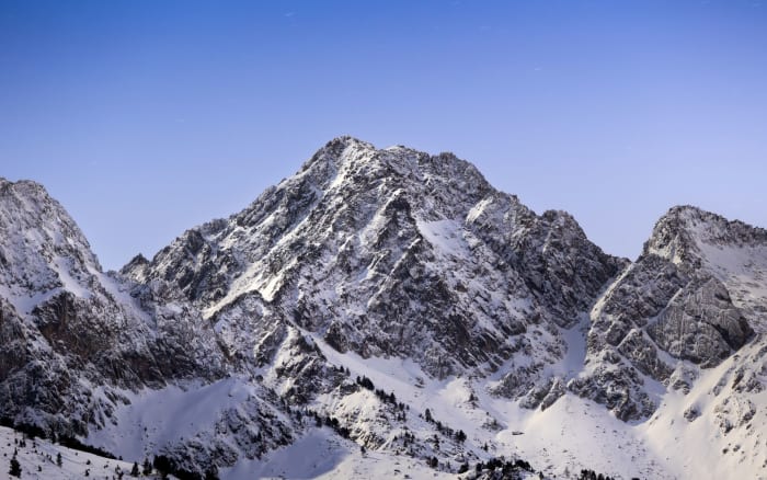 Breathtaking view of snow-covered mountains under a clear blue sky at sunrise, capturing winter's serene beauty.