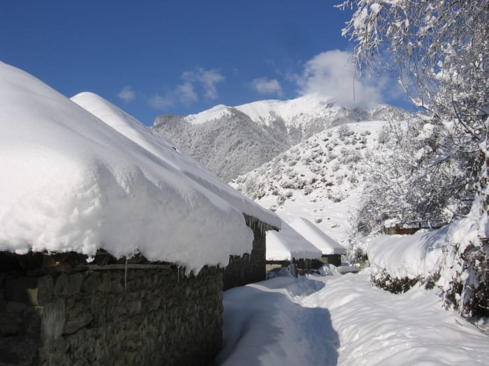 Idyllic snow-covered village with mountains under a clear blue sky in winter.