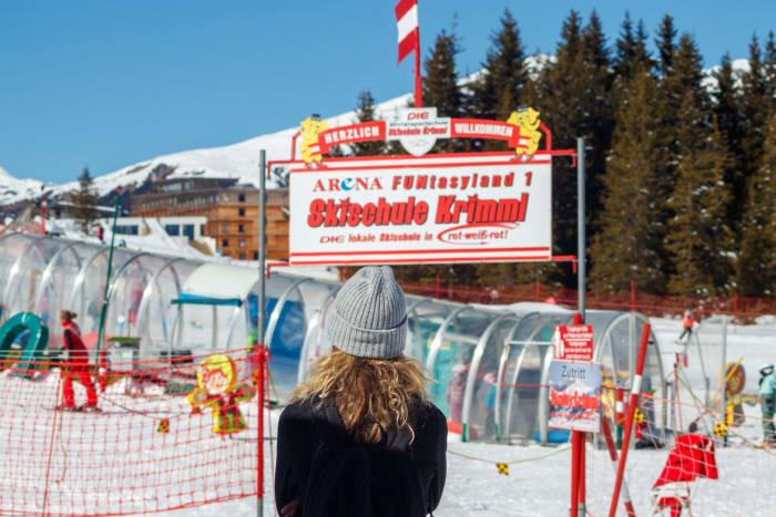 Woman standing at ski school entrance in snowy Krimml, Austria during winter.