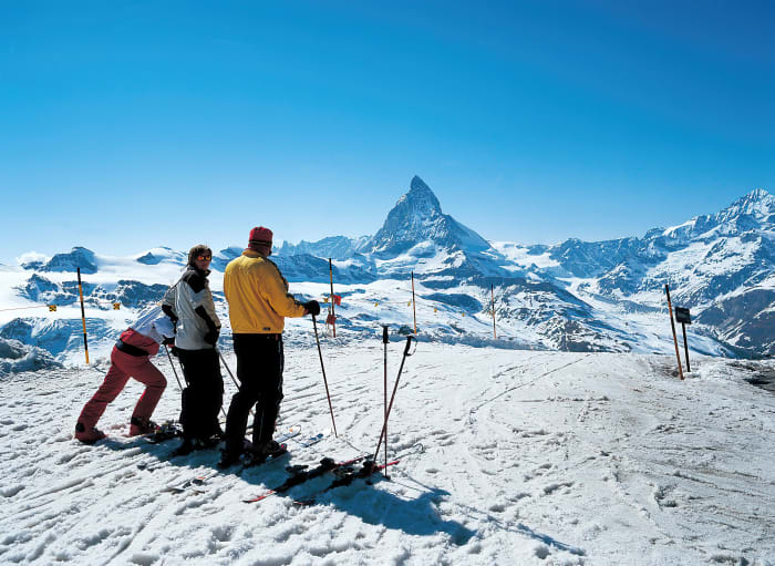 Three skiers on a snowy ridge looking towards the Matterhorn