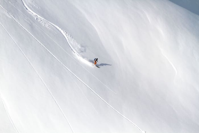 An aerial shot of a skier carving down a snow-covered mountain in winter, leaving a trail behind.