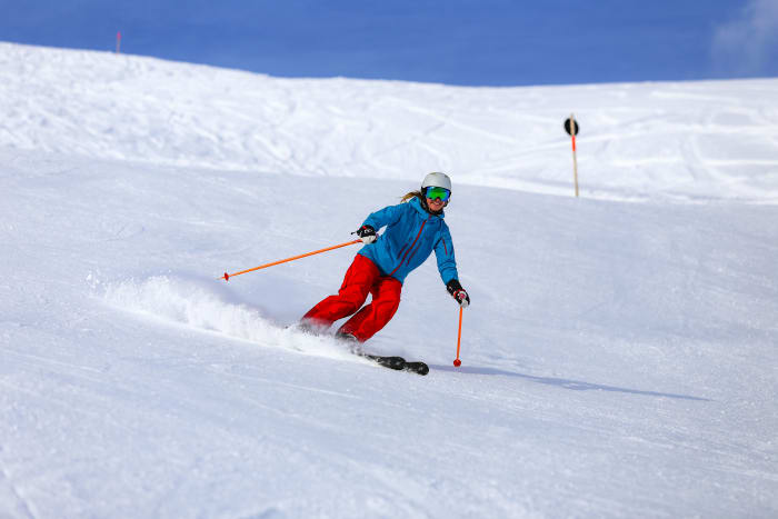 A skier in a blue jacket and red trousers carving a groomed slope in Vorarlberg