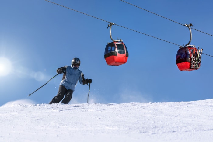 Skier on a snowy slope with gondolas against clear blue sky, capturing winter sport excitement.