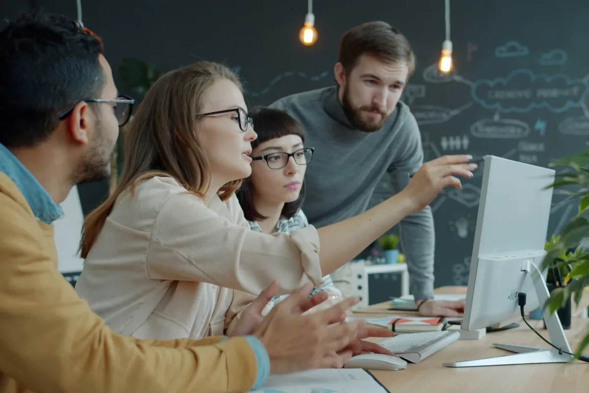 Petite équipe de développeurs échangeant autour d'un écran d'ordinateur dans un bureau, discussion technique en petit groupe