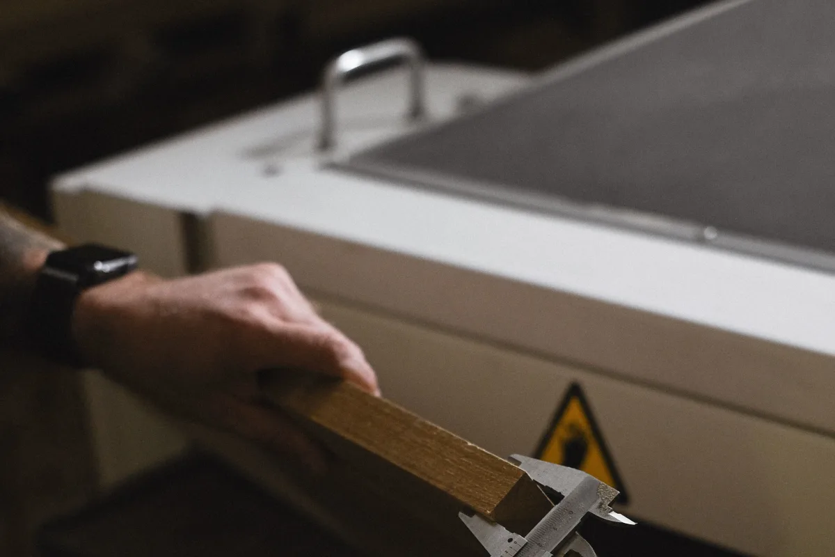 Artisan mesurant une pièce de bois au pied à coulisse avec précision, symbolisant le travail sur mesure d'une équipe spécialisée