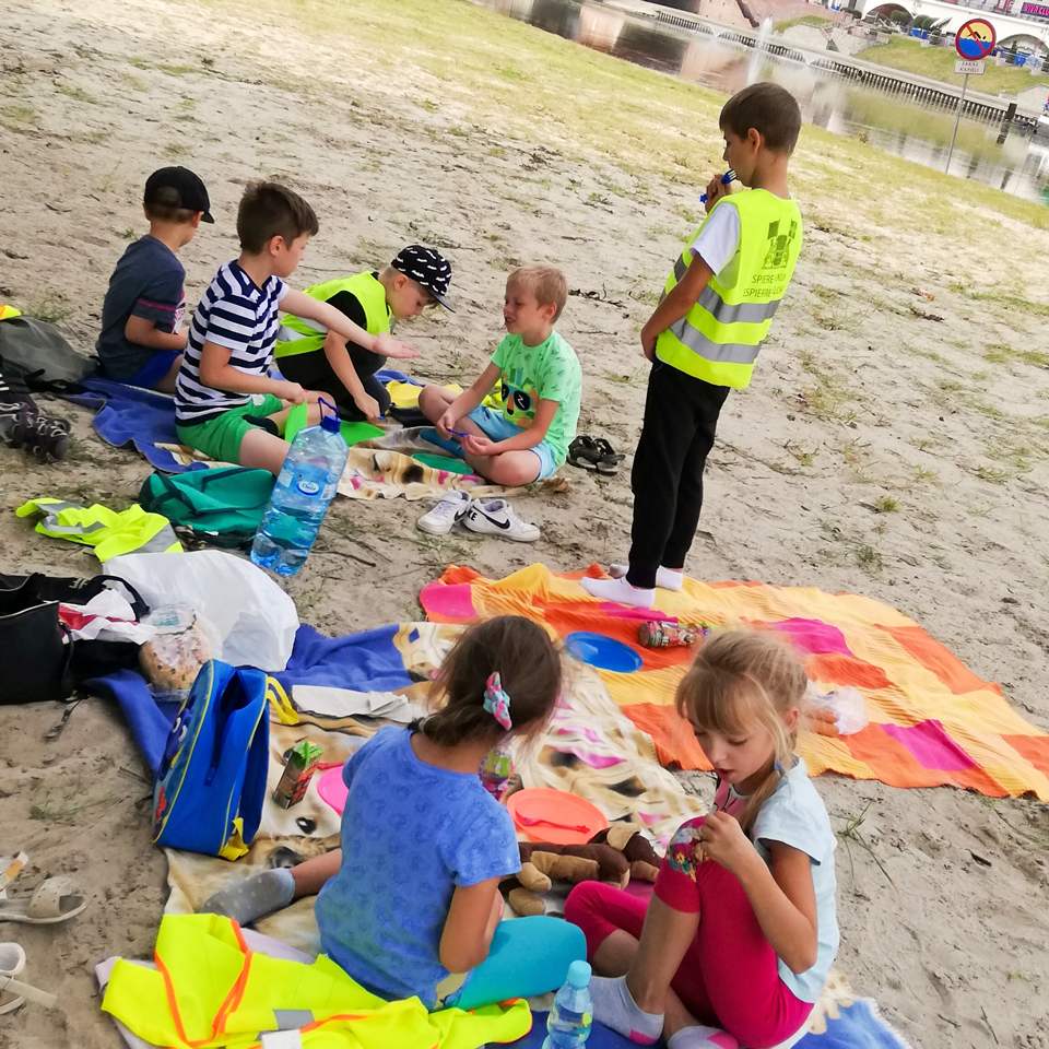 Dzieci siedzą na kocach rozłożonych na piasku plaży