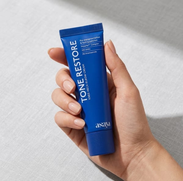 World of Asaya Tone Restore Knee-Neck-Elbow Cream held in hand, candid photo