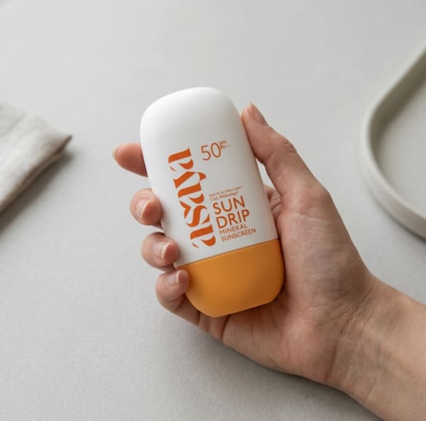 World of Asaya Sun Drip Mineral Sunscreen held in hand, candid photo