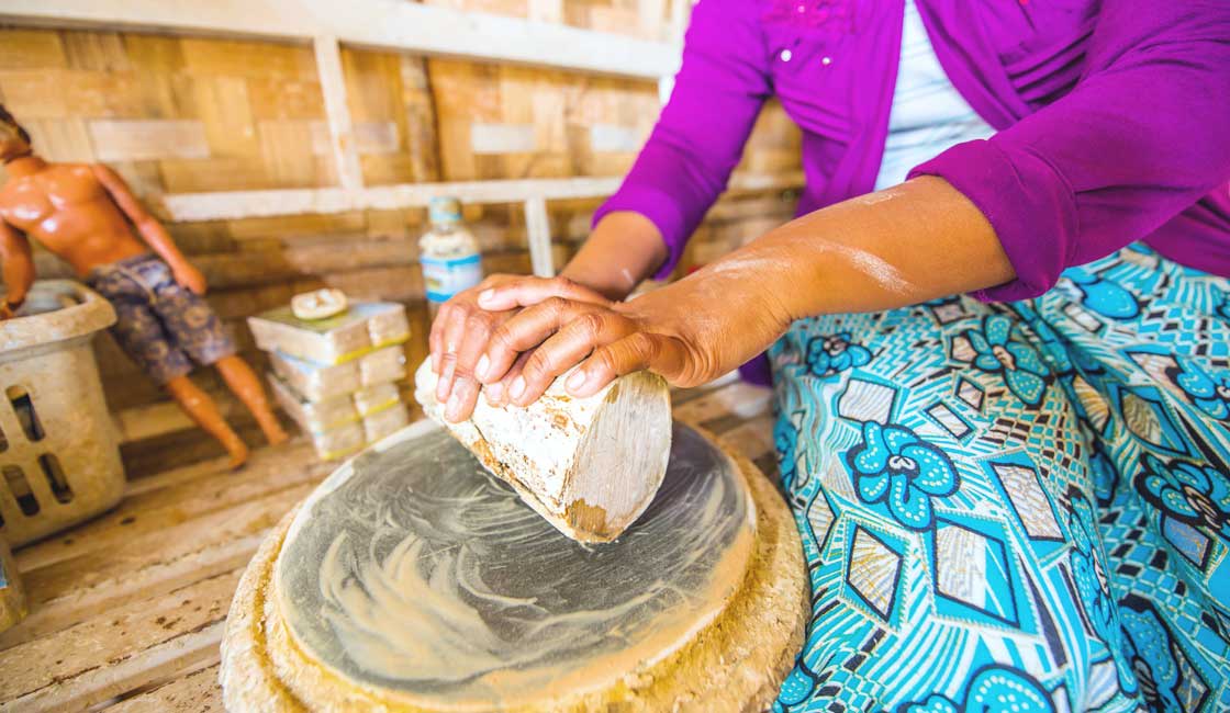 Hands rubbing thanaka wood chunk against a stone slab