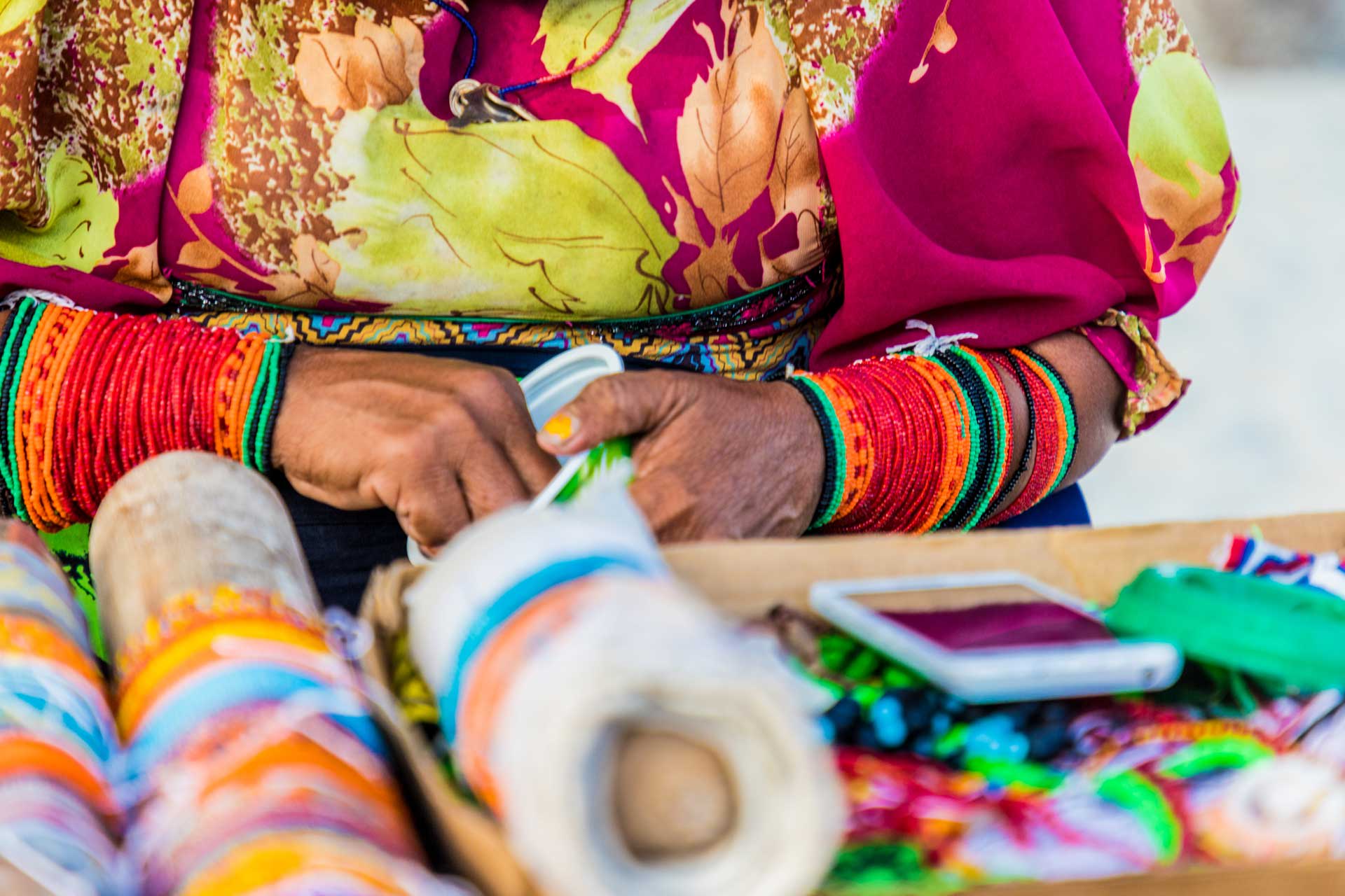 Close-up of a Guna woman's hands wearing traditional colorful beaded arm cuffs while working with craft materials.
