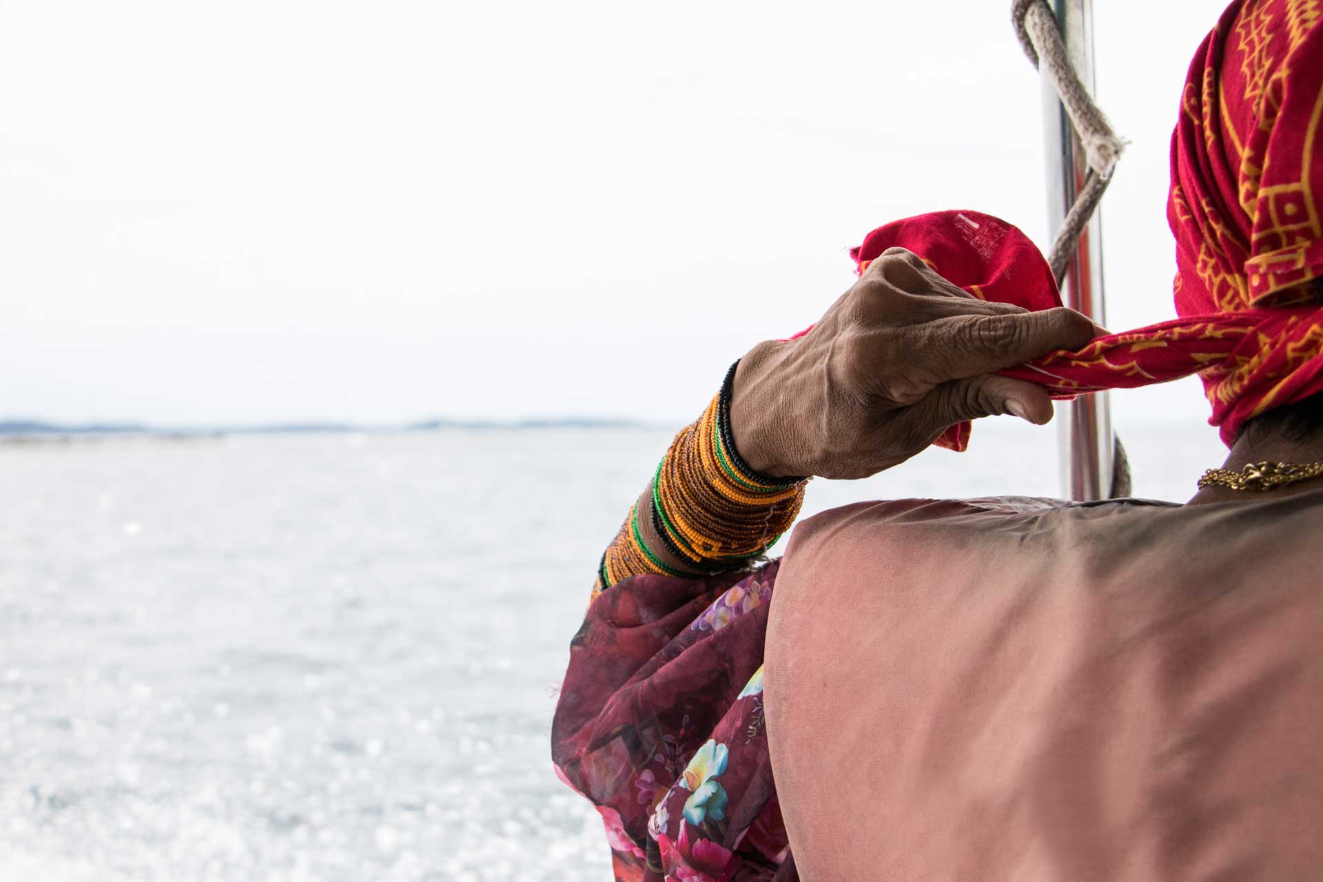 Rear view of a Guna woman in a red headscarf and beaded arm cuffs looking out over a vast body of water.