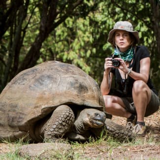 A woman with a camera kneeling next to a large tortoise