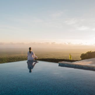 A woman meditating by the infinity pool