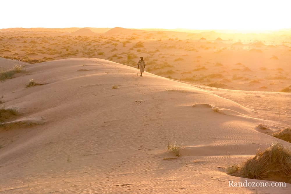 Un berger marche sur les dunes dans le soleil couchant