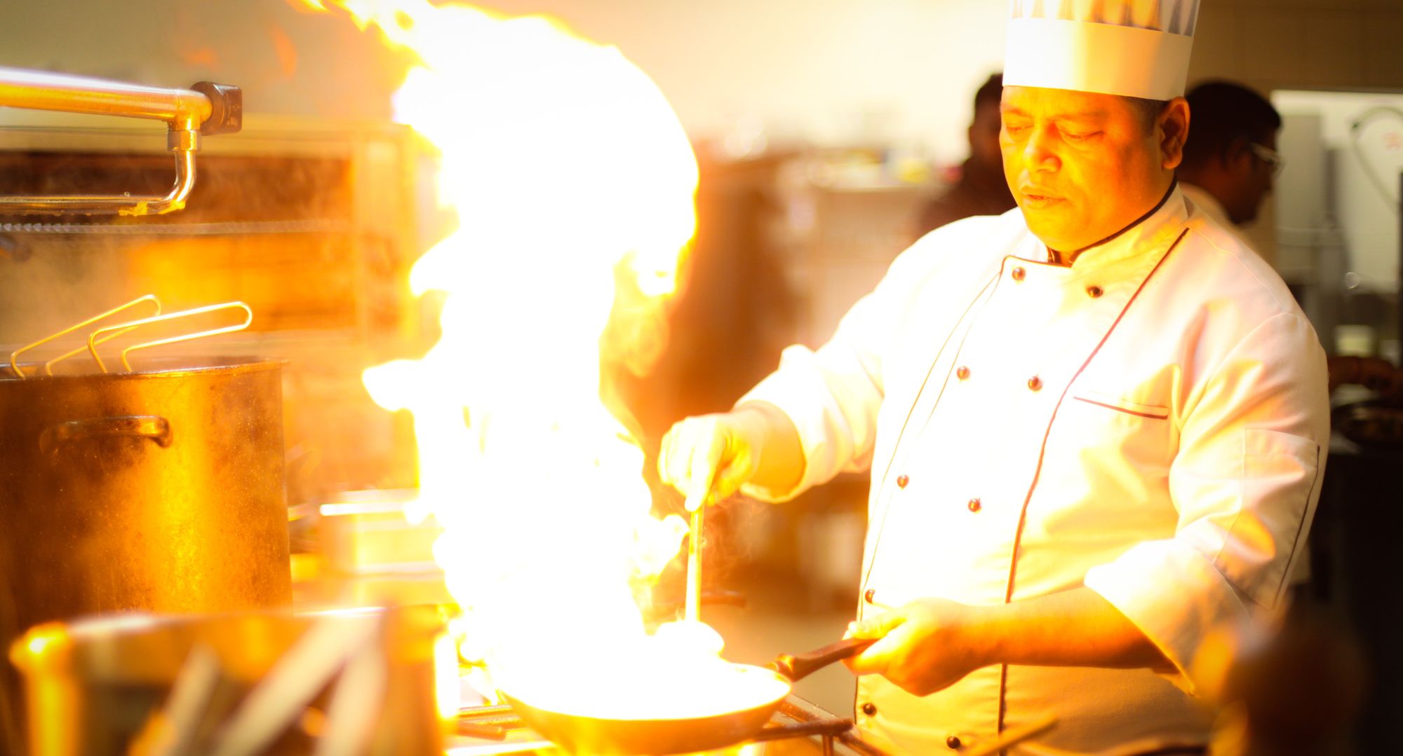 A chef manages a large fire in his pan.