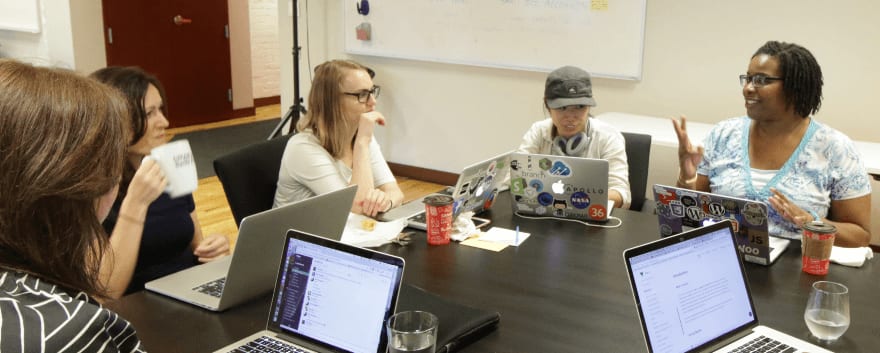 Bridge students discussing at a table with laptops open