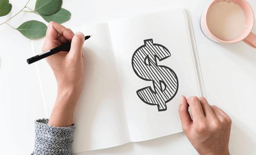 person drawing money symbol in notebook