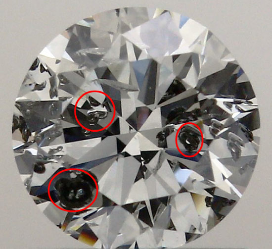 A round diamond against a gray background with very large black crystals circled in three places