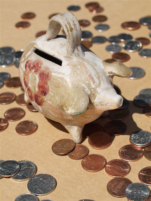 A rustic piggy bank displayed on a beige surface, with pennies scattered around it