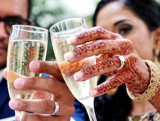 Photo of an Indian couple toasting with wedding rings on and henna tattoos on the brides hand