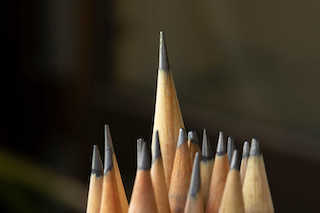 Image of a collection of sharpened graphite pencils with one standing higher than the others