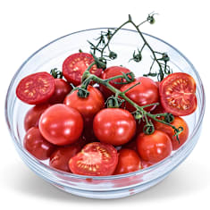 A clear glass bowl full of Chadwick Cherry Tomatoes on a white background.