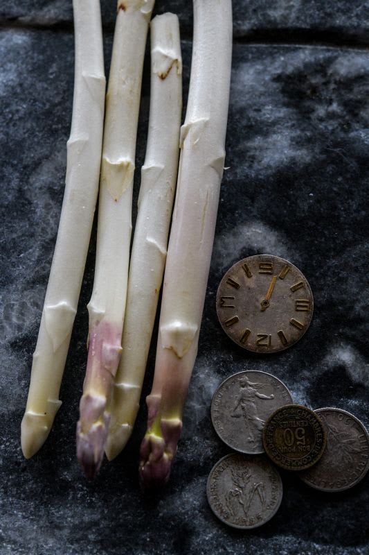 Spears of white asparagus with coins on blue background