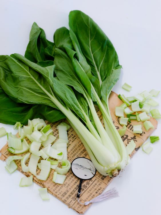 A large head of bok choy (Snow White) on a cutting board surrounded by chopped pieces of bok choy