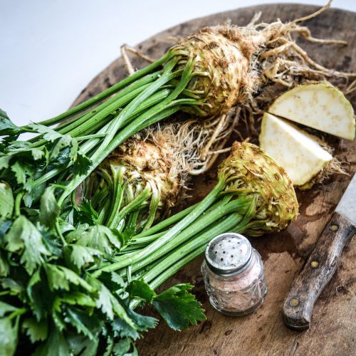 Celeriac (celery root) cut into pieces on a wooden board with knife