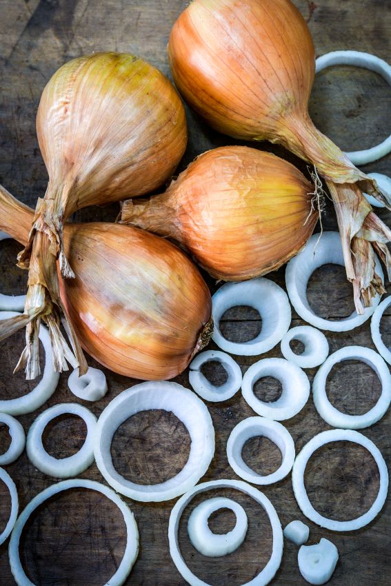Four large onions on a wooden board with rings of onion around them