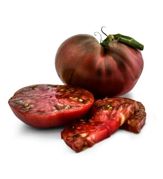 A large, dark red heirloom tomato called Cherokee Purple, with slices of the tomato on a white background