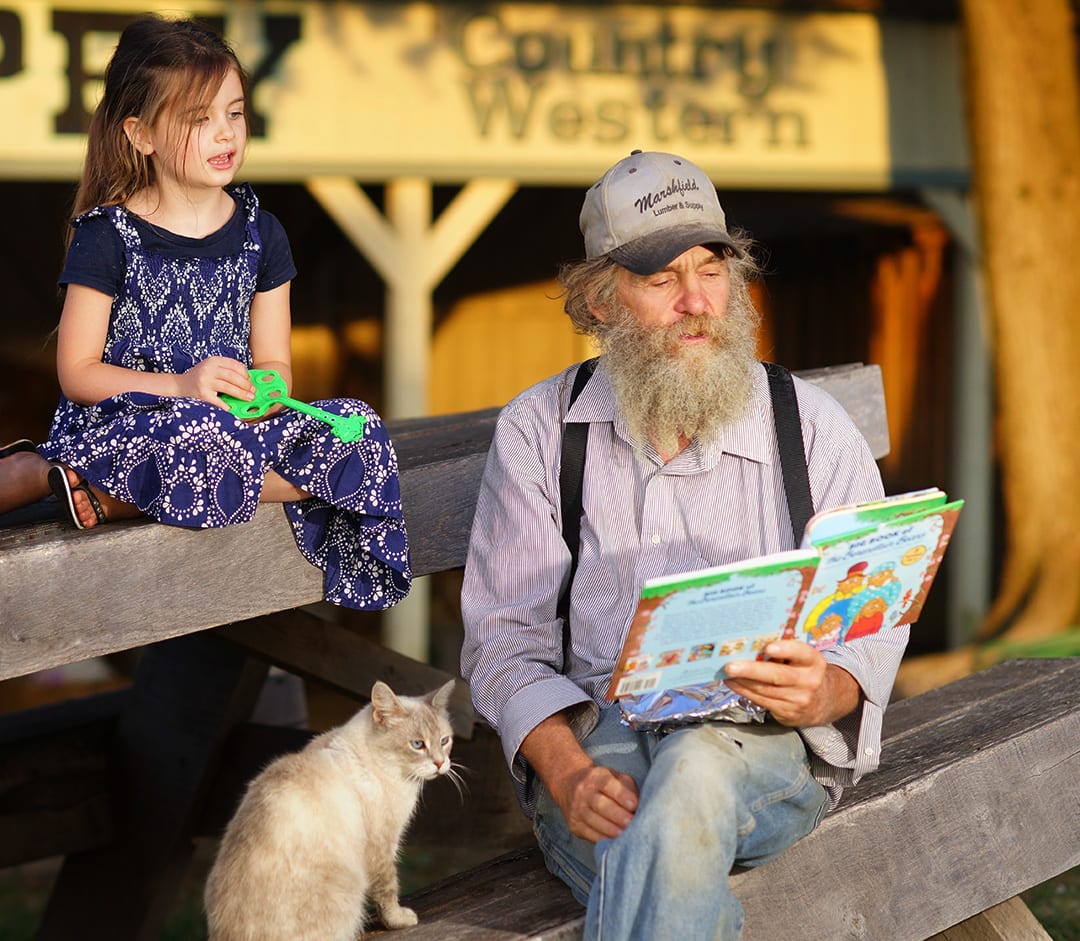 Dave reads a picture book to young Sasha Gettle as a cream-and-grey cat with blue eyes looks on