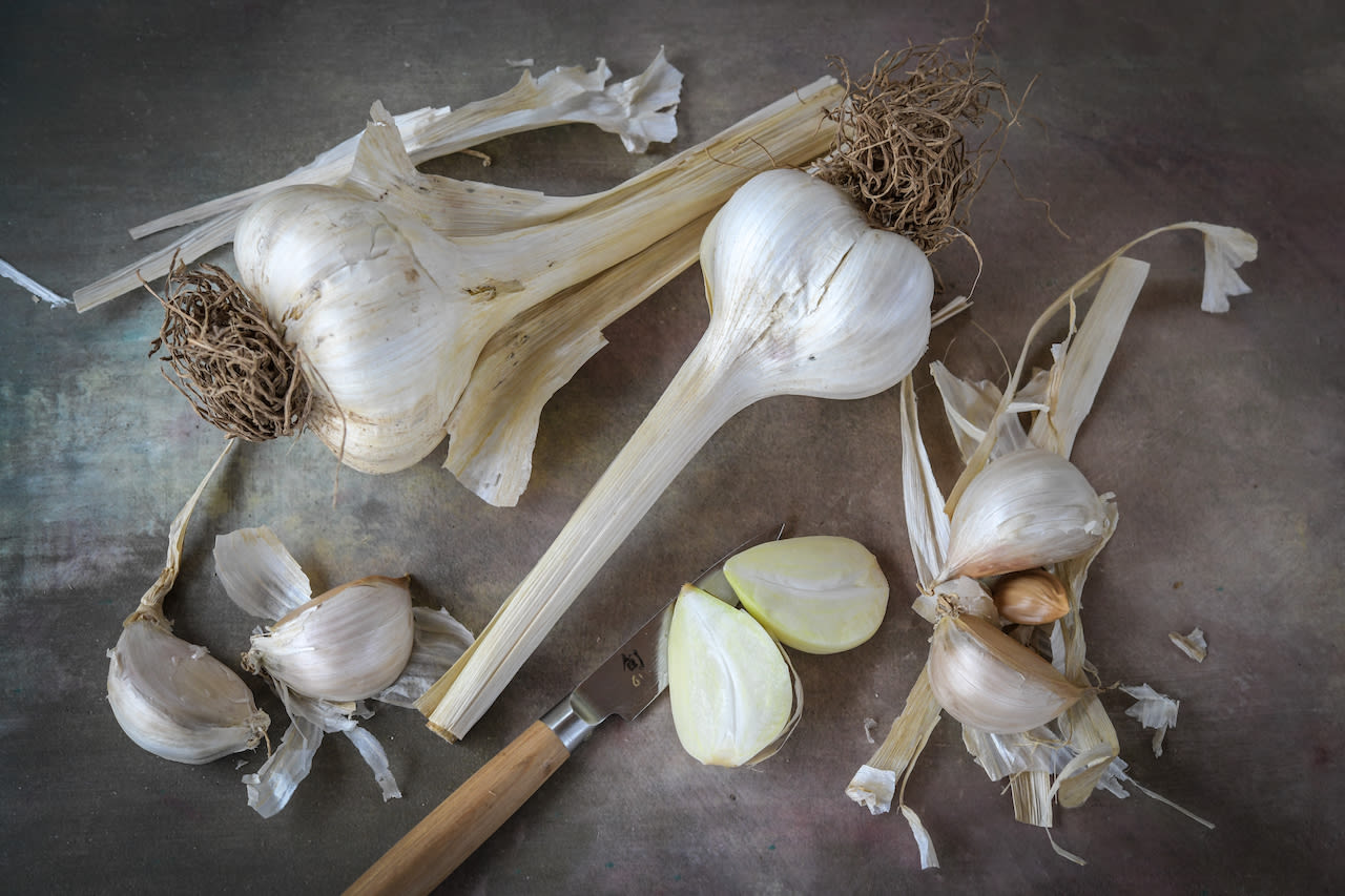 Several whole garlic heads, some individual cloves and a wooden handled knife on a board.