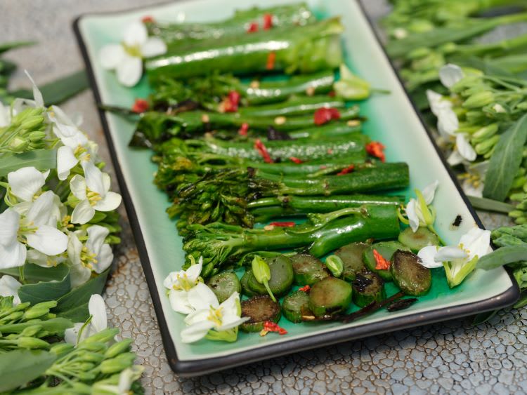 rectangular serving plate in center holds sauteed Yod Fah and is surrounded by flowering stems