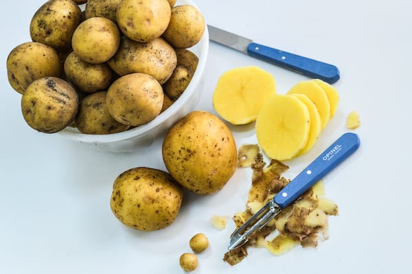 Yukon Gold potatoes in bowl with sliced potatoes, paring knives, and microtubers in front