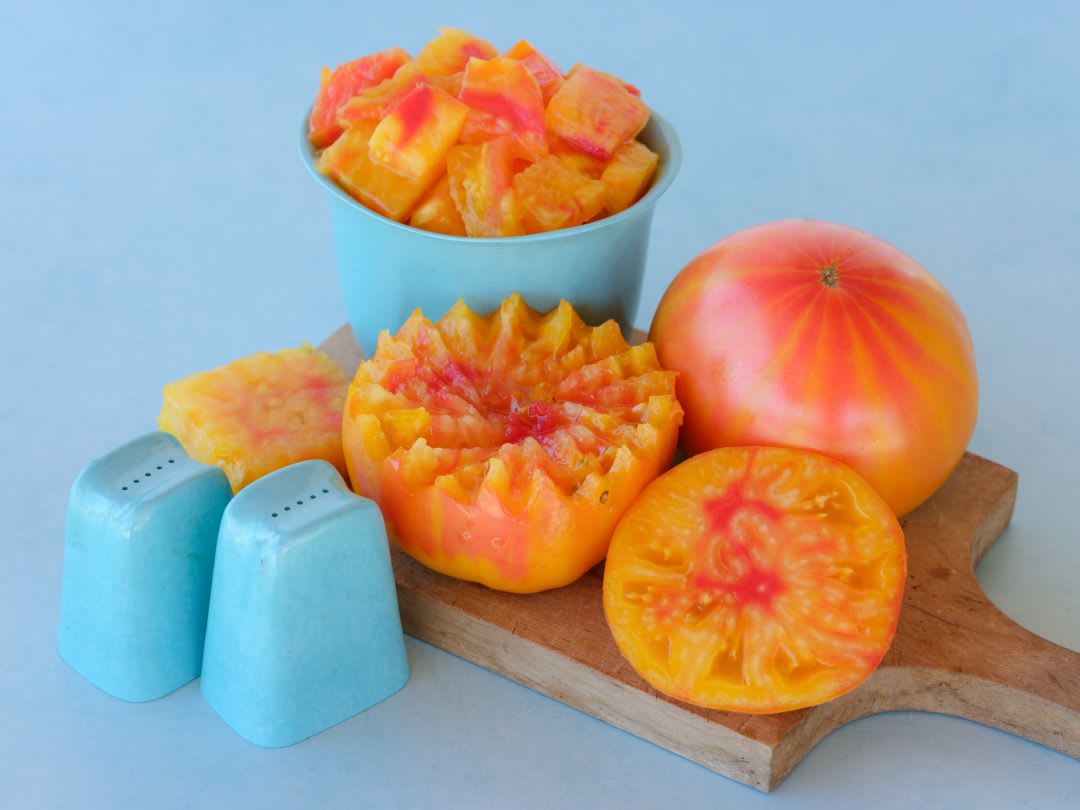Orange tomatoes on wooden cutting board with pale turquoise salt & pepper shakers