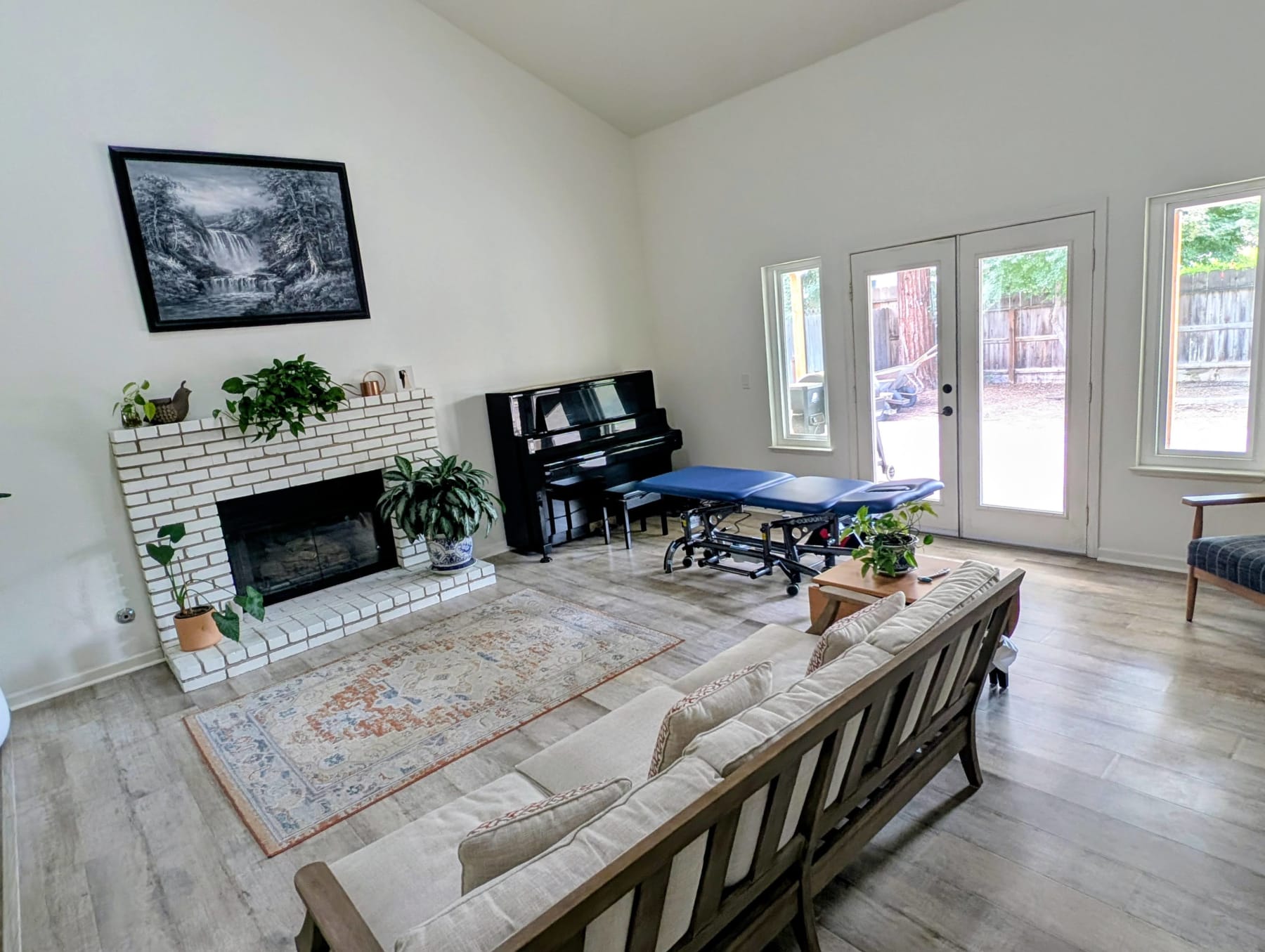 The treatment room: a treatment table by tall windows, a fireplace, a piano and plants