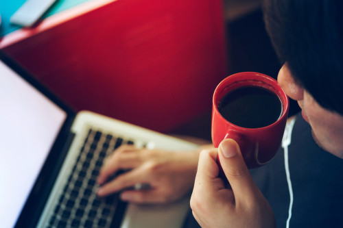 Person med kaffekopp framför datorn.