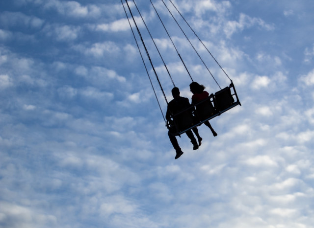 Två personer i en slänggunga högt uppe i himlen.