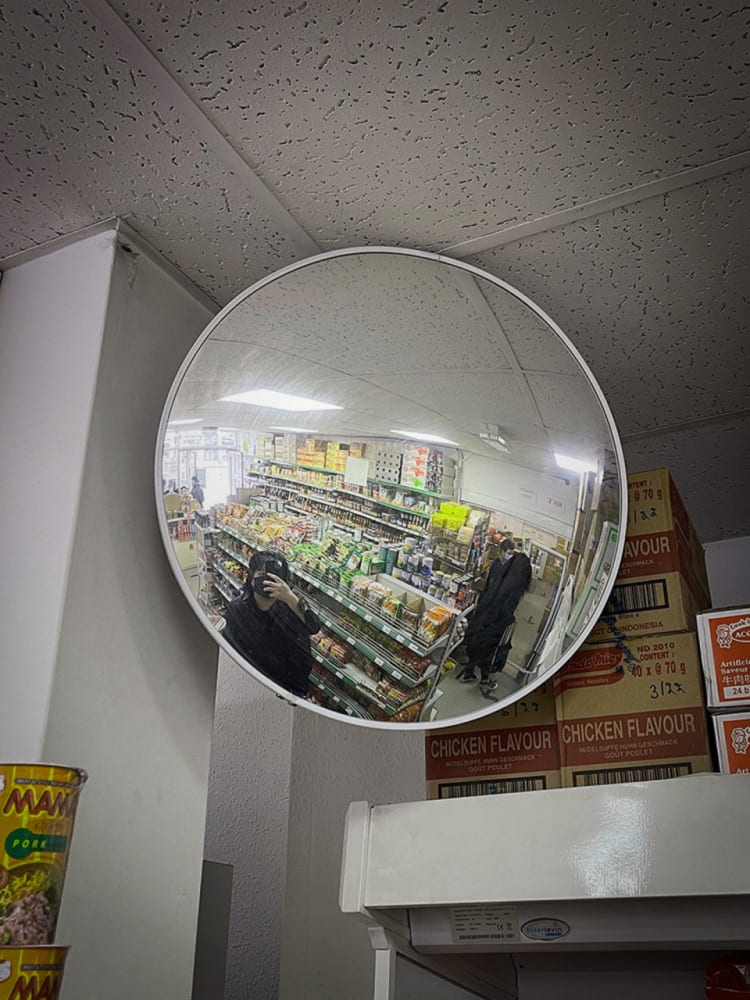 Large reflective oculus, reflecting the distorted interior of an asian supermarket. A person can also be seen taking photo of it