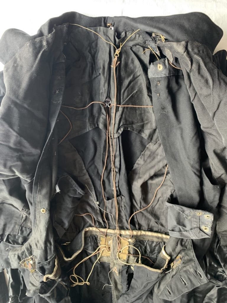 Upper body of a creased black evening suit, opened to show internal network of strings for quick-change functionality.