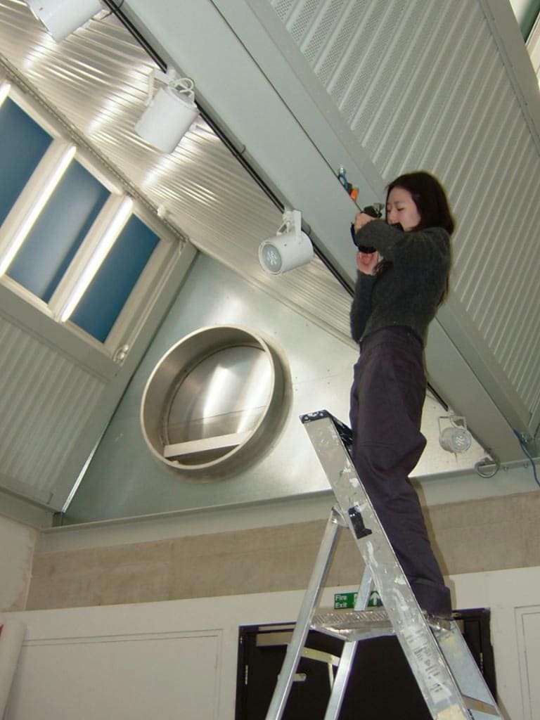 Myungmin Liu is standing on top of the ladder in the studio, checking her camera.